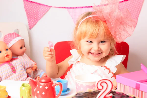 Happy cute little girl with sweets and dolls at birthday