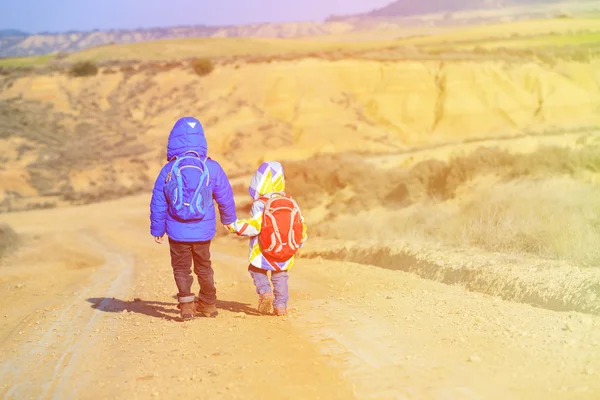 Little boy and girl with backpacks travel on the road to mountains