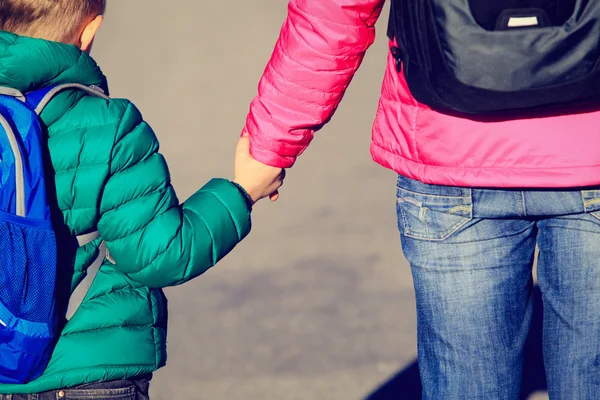 Mother holding hand of little son with backpack on the road