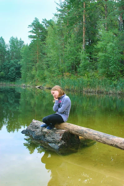 Beautiful girl sits on the log by the river