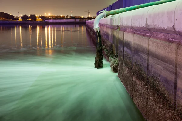 Sewage pipe discharging water into a river at night. Dubai Creek, UAE