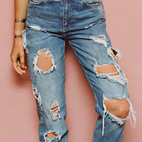 Lady in fashionable ripped jeans stands in pink wall