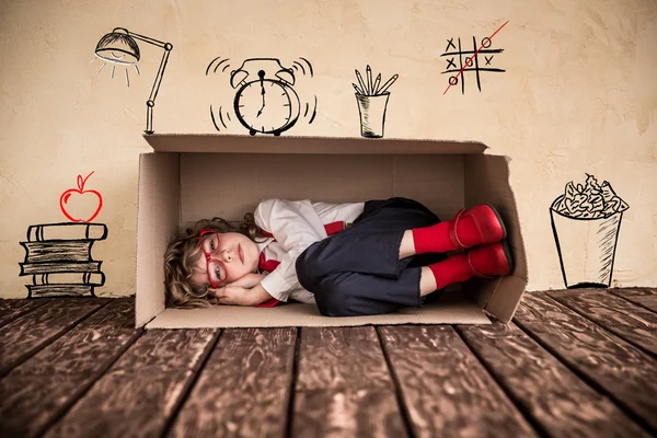 Child businessman sleeping in cardboard box.