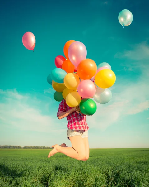 Woman jumping with toy balloons in spring field