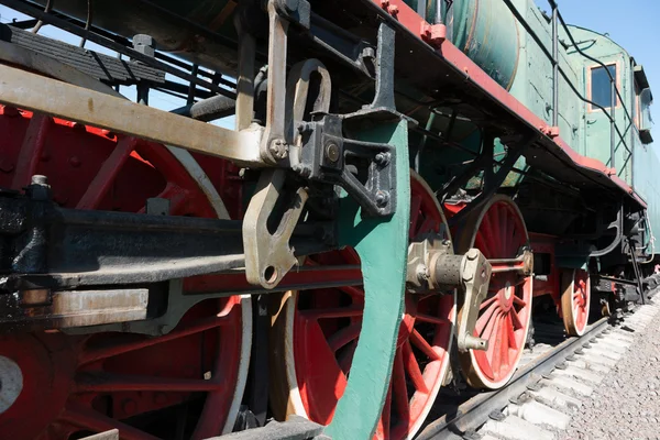 Partial view of a steam locomotive. Green metal boiler, red wheels