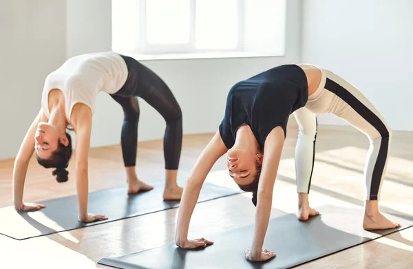 Two young women doing yoga asana upward bow (wheel) pose