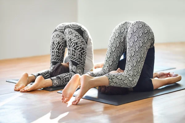 Two young women doing yoga asana easy plow pose