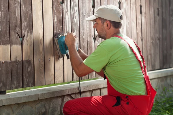 Worker sanding away old paint from a wooden fence