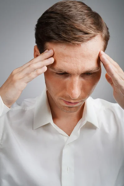 Young man in white shirt thinking or experiencing headaches.