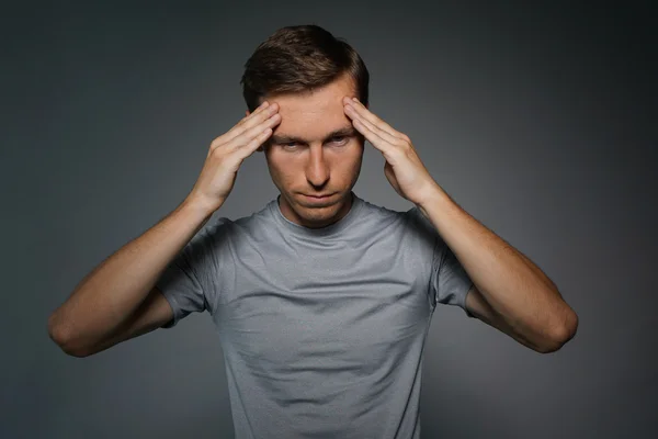 Young man in t-shirt thinking or experiencing headaches.