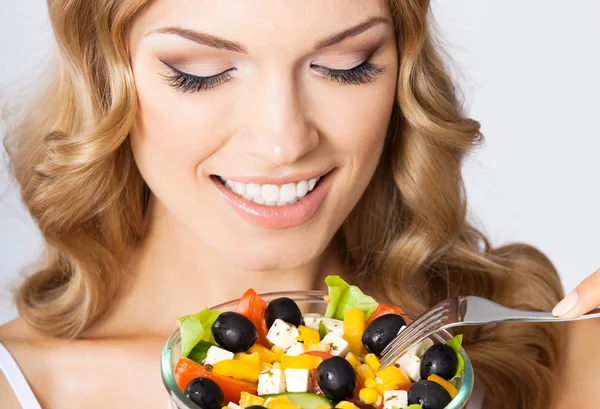 Portrait of young woman with vegetarian salad, on grey