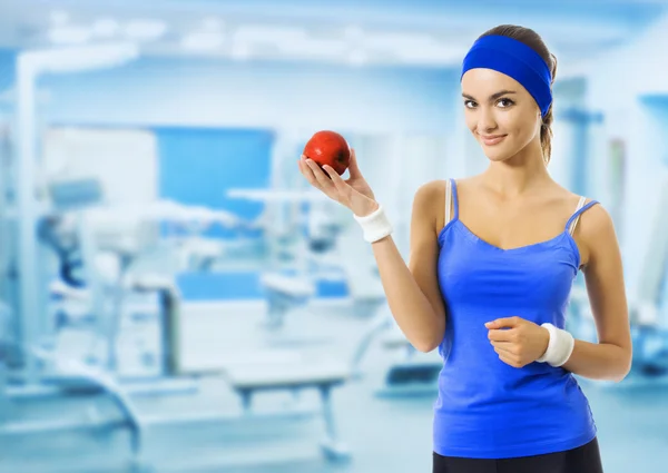 Woman in sportswear with red apple, at gym