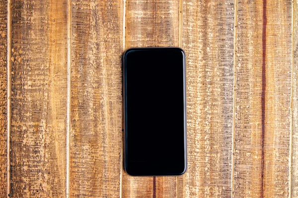 Blank black phone on wooden desktop. Topview, Mock up