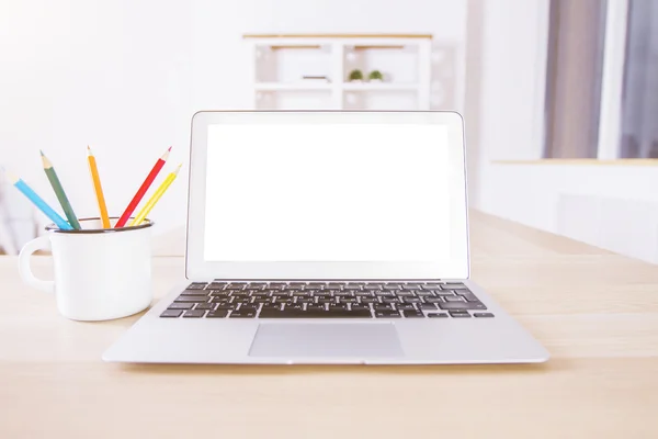 Blank white laptop screen on wooden desktop with pencils in iron mug. Mock up