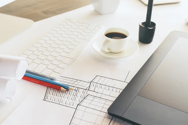 Closeup of tabletop with construction sketch, graphic tablet, coffee cup and other items