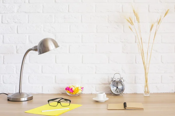 Creative desktop with glasses, coffee cup, lamp, stationery and other items on white brick wall background