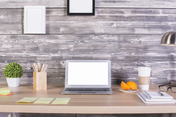 Closeup of modern designer workplace with blank white laptop, stationery items, orange slices, coffee cup, picture frames above and other objects. Mock up