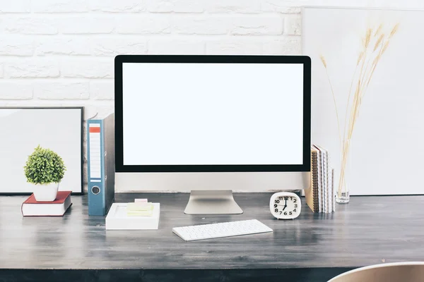 Creative designer desktop with blank white computer monitor, keyboard, stationery items, decorative plants and blank picture frames on white brick wall background.