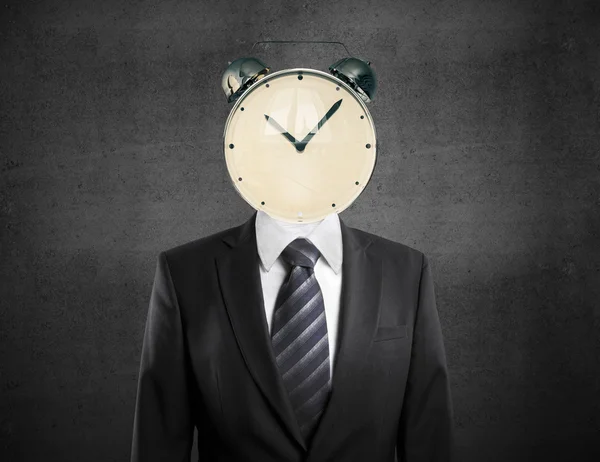 Time management concept with alarm clock headed businessman on concrete background