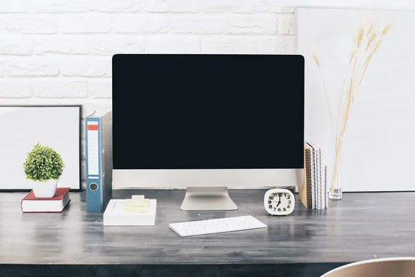 Creative designer desktop with blank computer monitor, keyboard, stationery items, decorative plants and blank picture frames on white brick wall background. Mock up