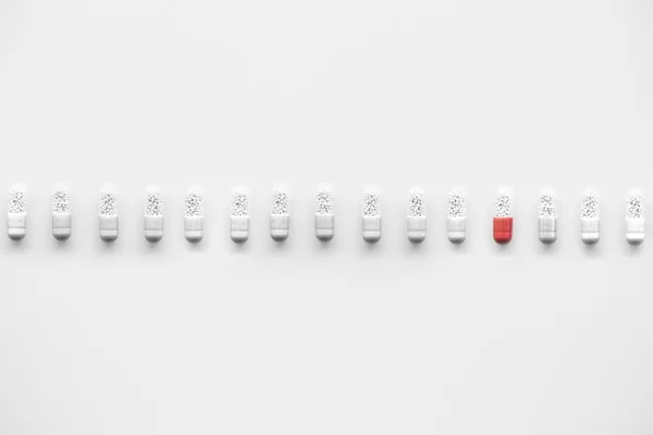 Row of white medication capsules with a standing out red one on light background