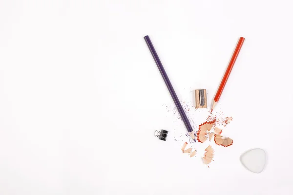 Top view of white desktop with pencils, sharpener, sawdust, small peg and eraser