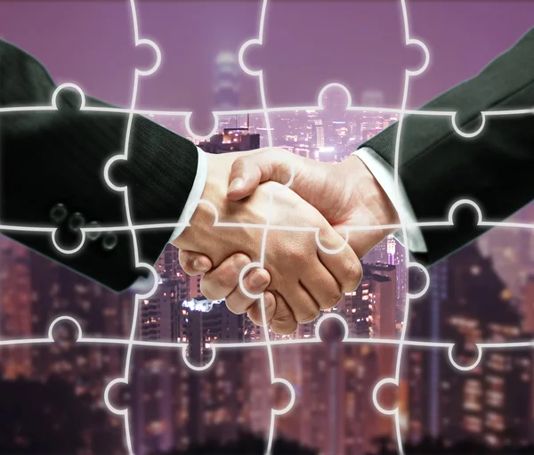 Businesspeople shaking hands on night city background with puzzle piece pattern. Teamwork concept