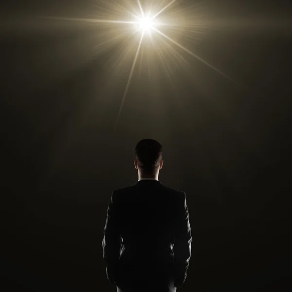 Back view of young businessman in suit on dark background illuminated with a lamp.
