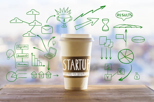 Startup concept with take away coffee cup and abstract business drawings on wooden desktop and blurry city view background