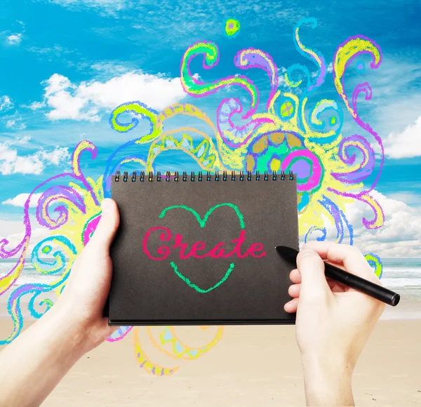 Male hand writing word create in black spiral notepad on abstract seashore background with creative colorful sketch