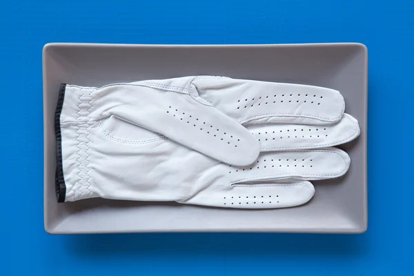 Gray ceramic dish with golf glove on over blue  background