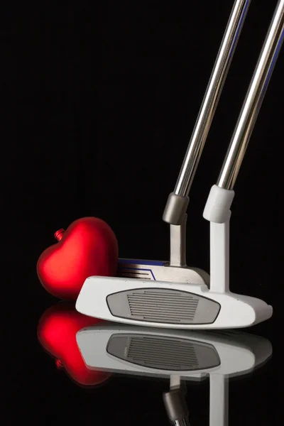 Two different golf putters and red heart
