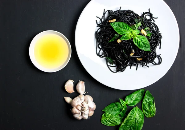 Black spaghetti with olive oil and garlic on black background