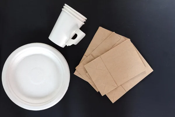 Paper plate, paper cup and brown paper bag on black background