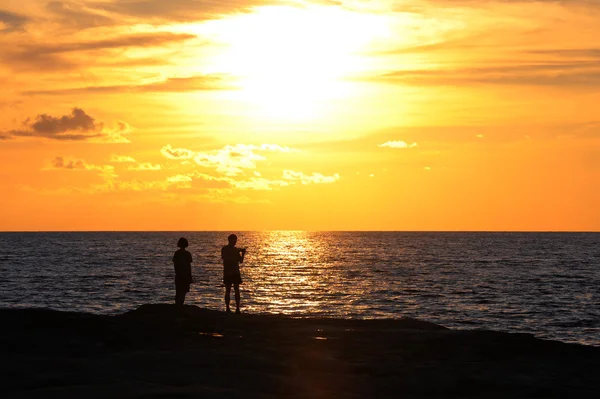 Young couple standing on the shore and looks at the setting sun