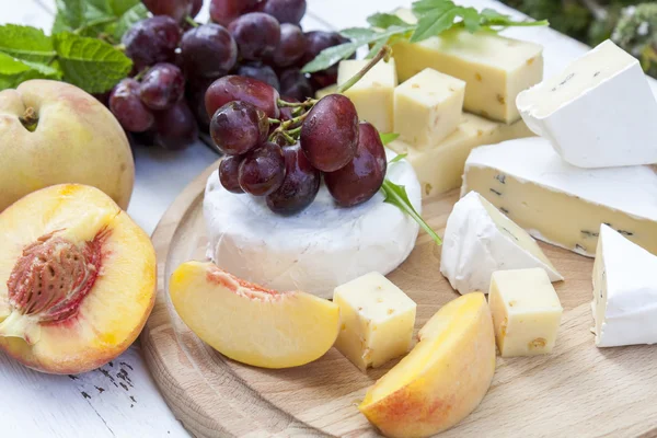 Different delicious cheeses and fruits on wooden round board