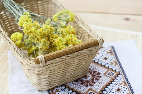 Dwarf everlast flowers bouquet in a wicker basket and napkin with embroidery on light wooden table, selective focus