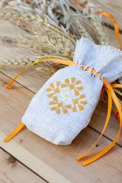 Sachet with ukrainian embroidery, wheat and oat on wooden background