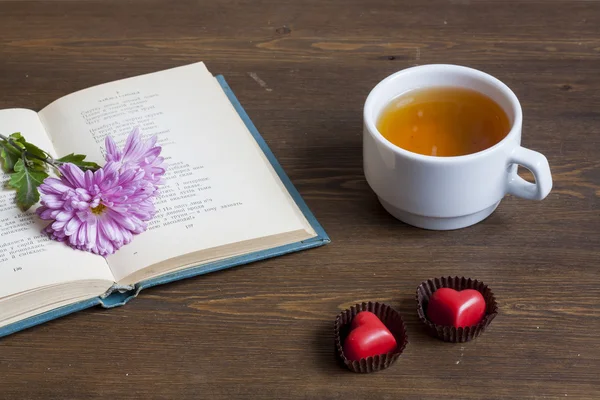 Cup of hot tea with books and flowers, red chocolate hearts