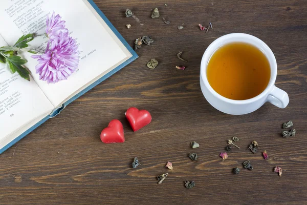 Cup of hot tea with books and flowers, red chocolate hearts and tea leaves