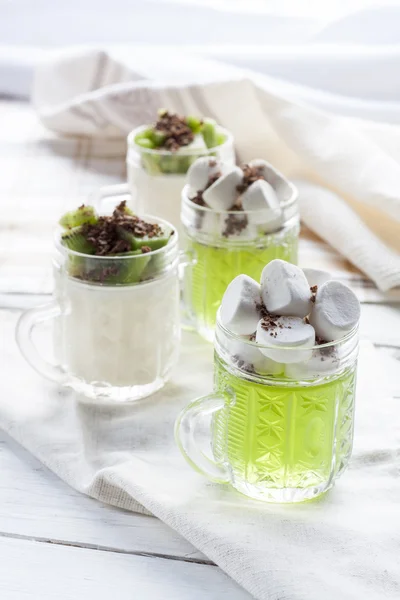 Jelly with kiwi fruit with marshmallows and grated chocolate in glass, sliced kiwi on white wooden table