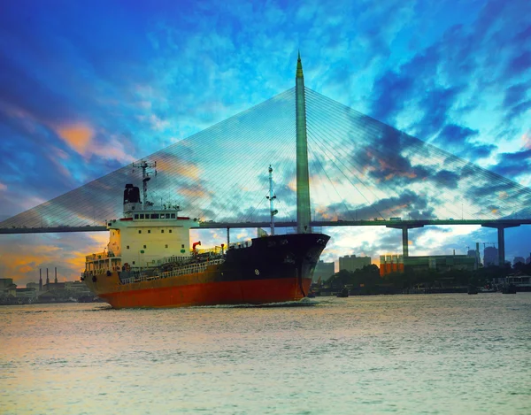 Tanker ship in river against beautiful bridge with twilight sky