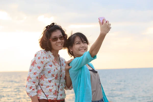 Two sister take a photo,selfie by smart phone beside sea beach w