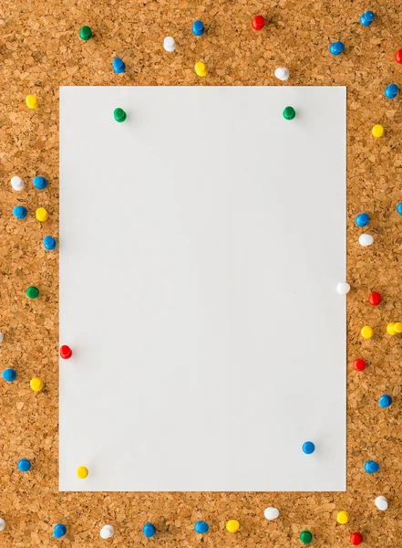 White paper note sheet with multicolored push pin on cork board