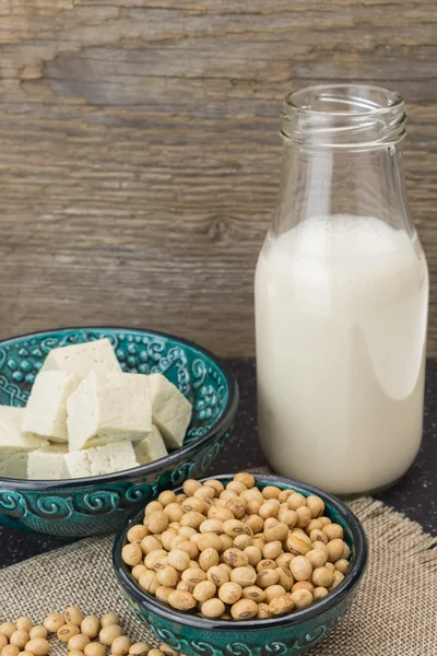 Tofu cut into cubes, soybeans in bowls and soy milk, on wooden background.
