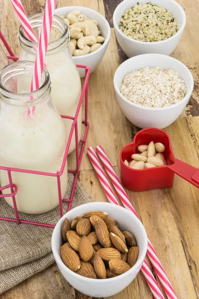 Bottles of homemade plant based milk and bowls with ingredients, on wooden background