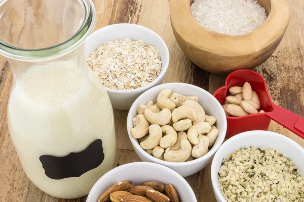 Bottle of homemade plant based milk and bowls with ingredients, on wooden background