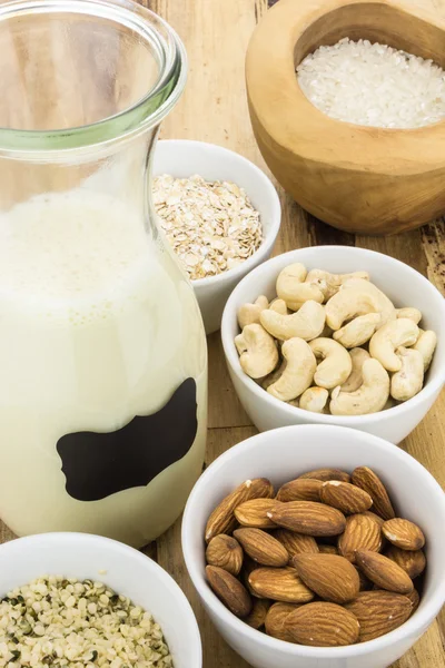 Bottle of homemade plant based milk and bowls with ingredients, on wooden background