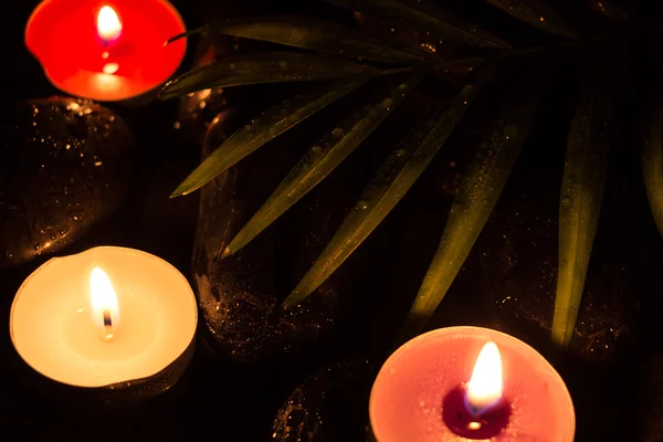 Scent colorful lighted candles on black wet stones and green leaf with droplets, dark photography