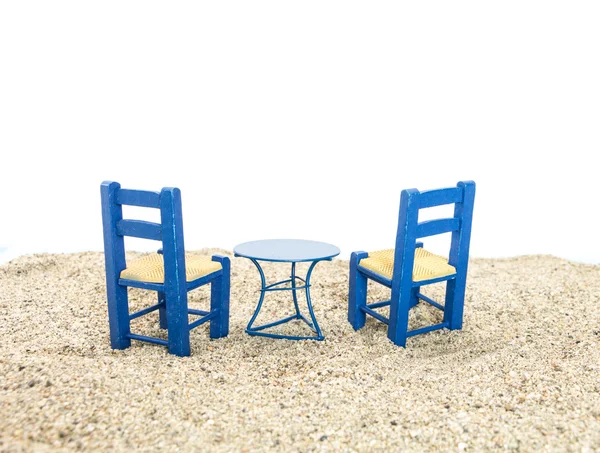 Blue painted chairs and table on sand, with white background.